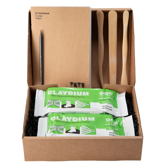 Open box showing kit contents: two blocks of air dry clay, three wooden tools and an a5 sketchbook.